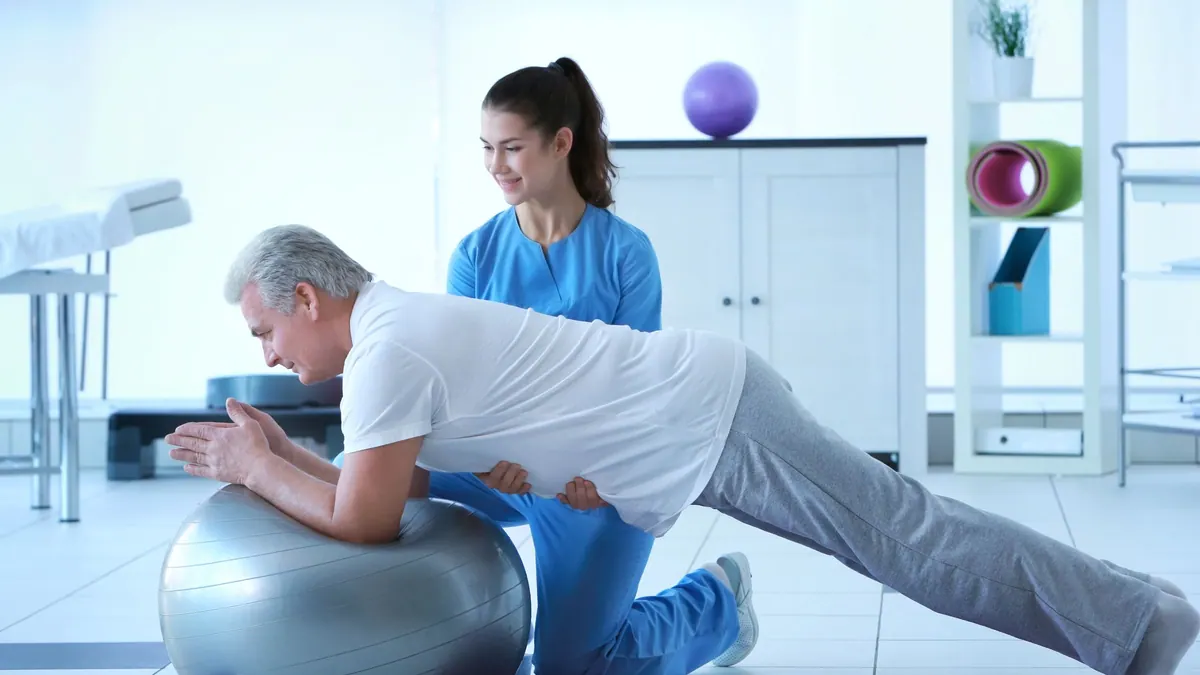 Fizyoterapi nedir: fizyoterapist klinikte egzersiz topu üzerindeki hastaya eşlik ediyor